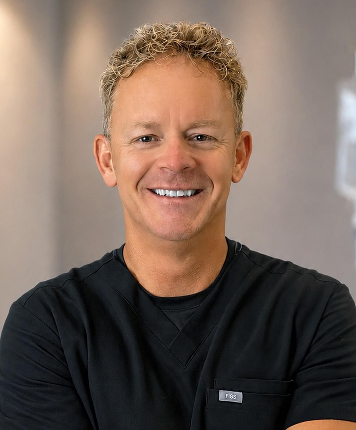 Smiling man in black scrubs with curly hair.