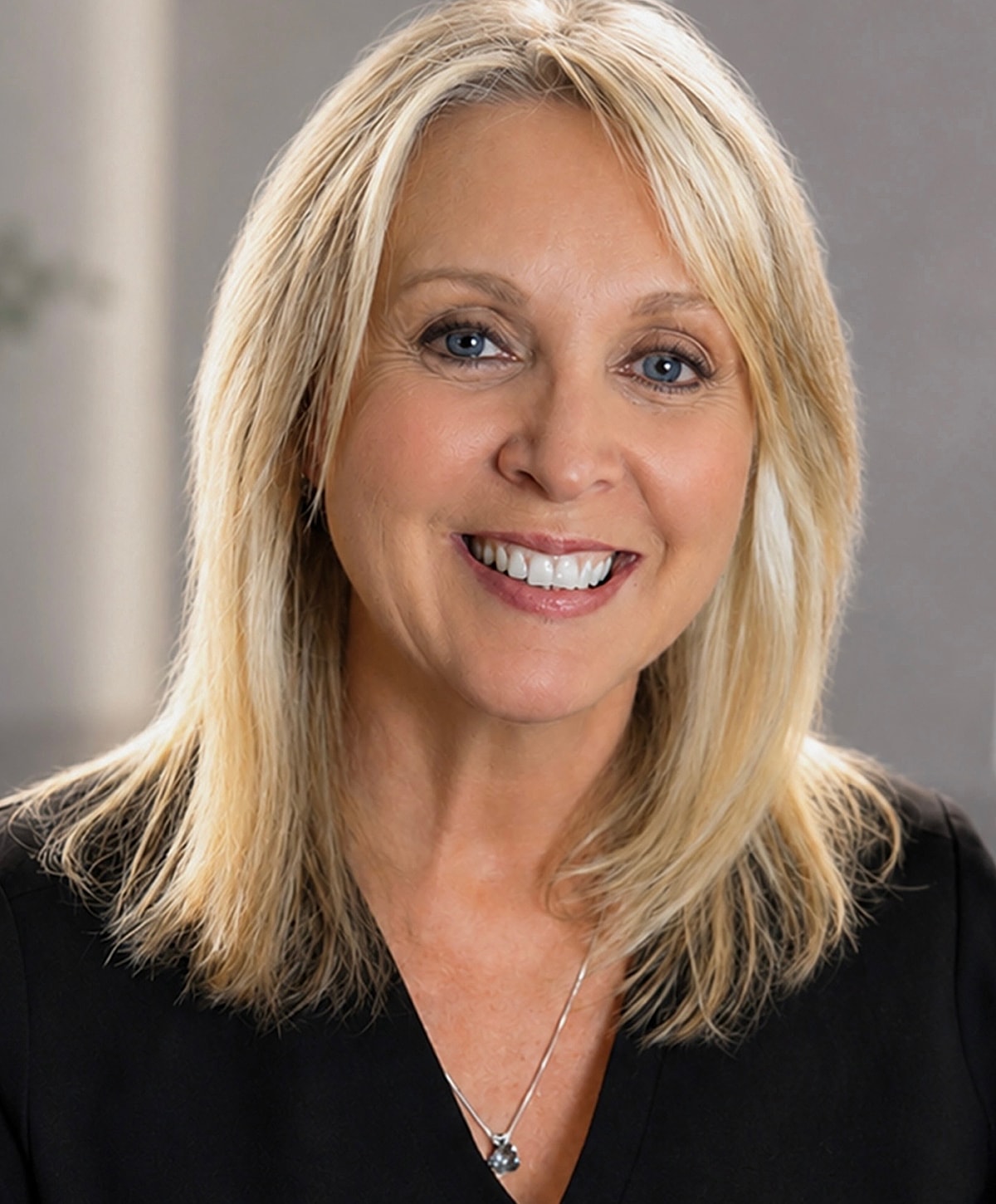 Smiling woman with blonde hair and necklace.